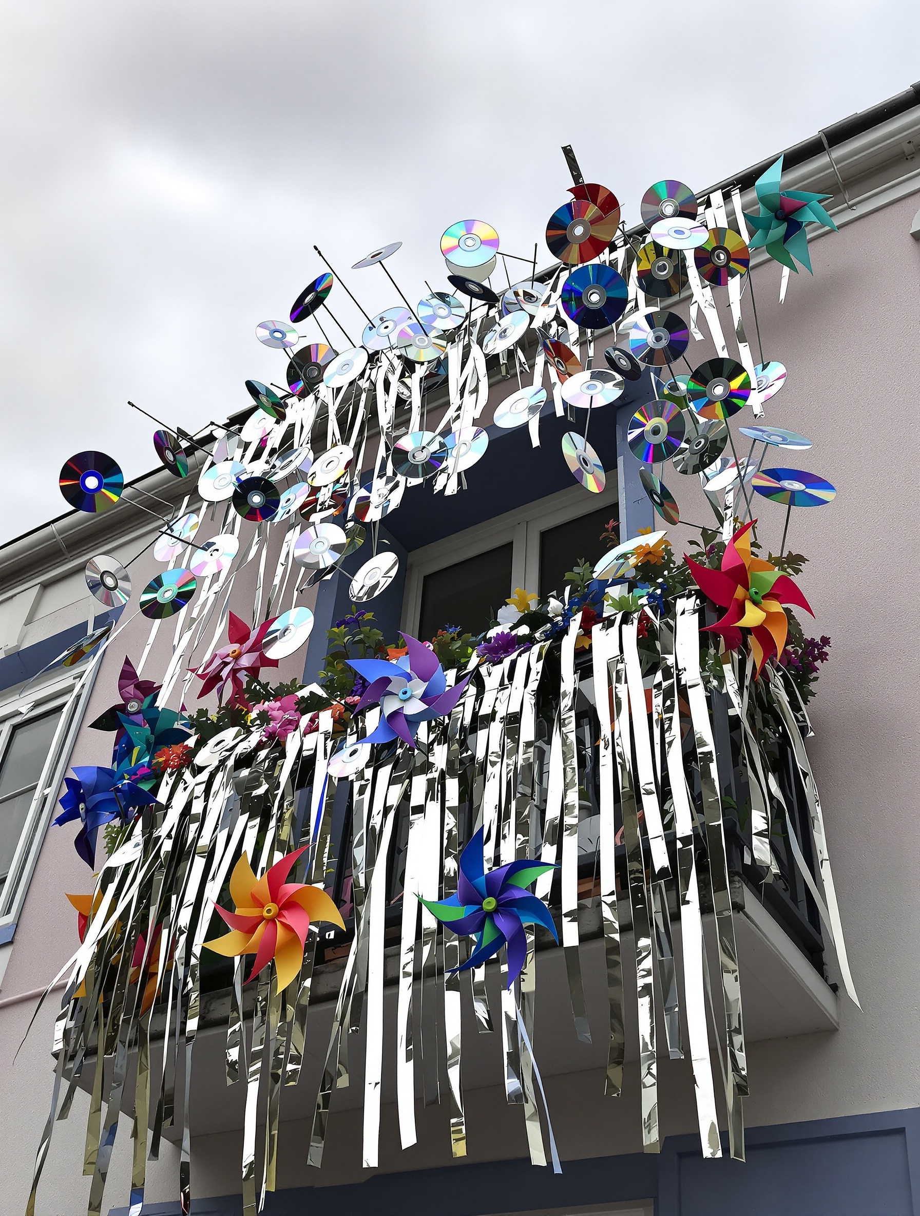 Balcon breton décoré de CD suspendus, bandes d'aluminium et moulins à vent colorés.