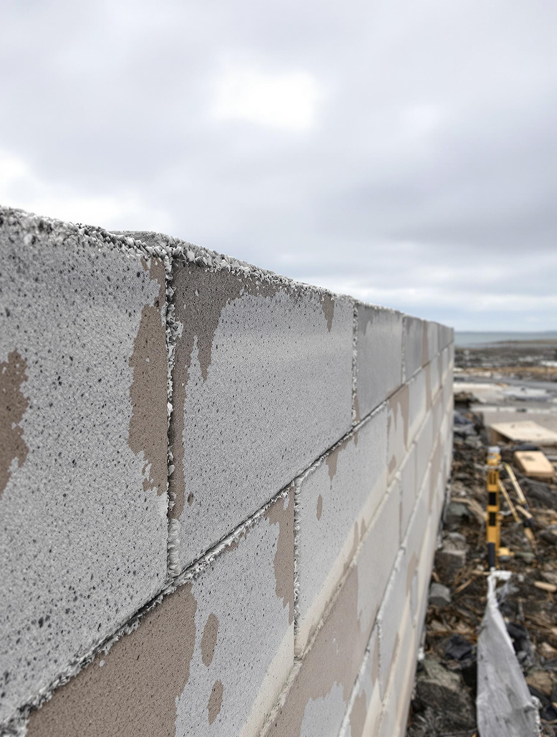 Mur acrotère rehaussé, joint mince, sous un ciel gris de la côte bretonne.
