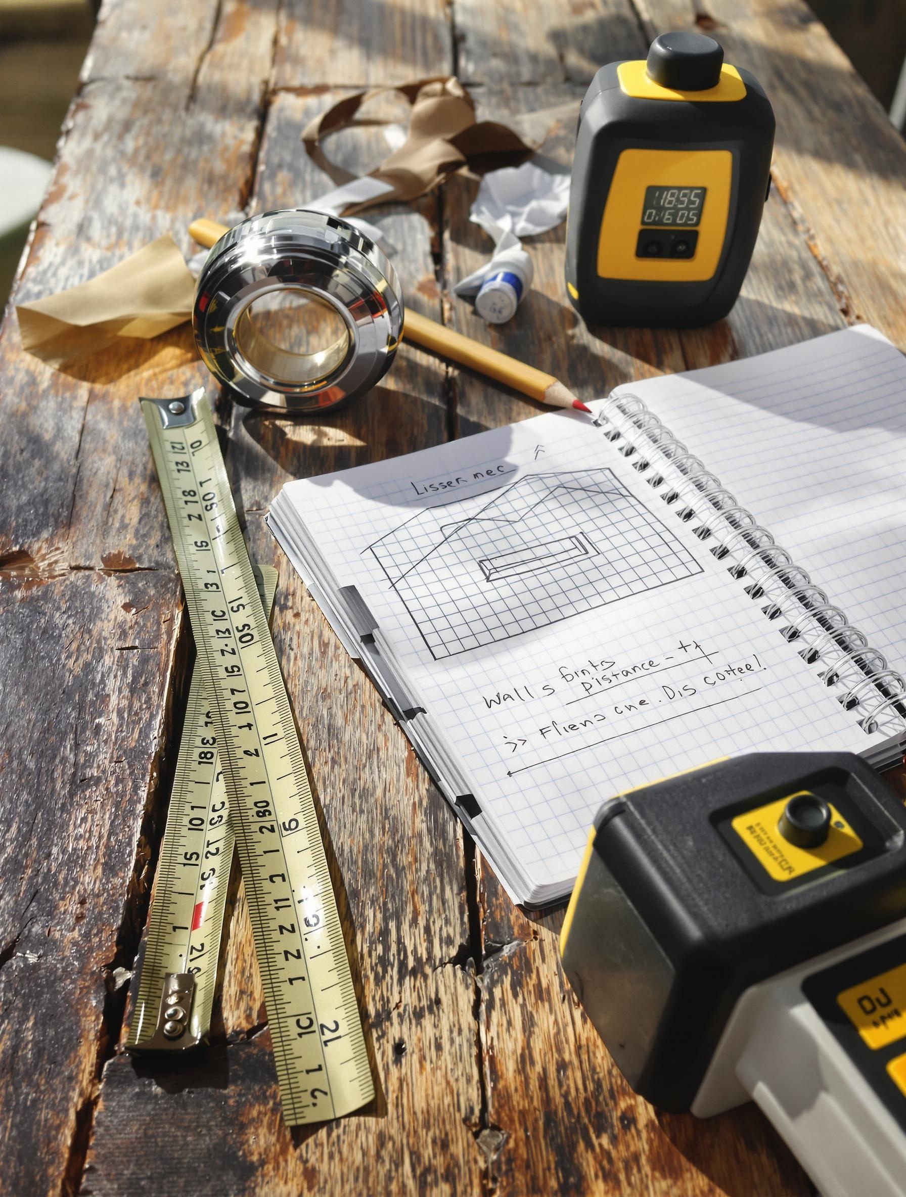 Outils de mesure pour calculer des surfaces murales : mètre ruban, carnet et télémètre laser.